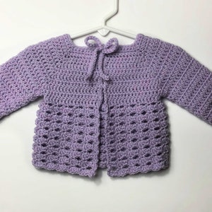 May include: A lavender crocheted baby cardigan with a tie closure at the neck.