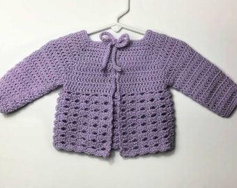 May include: A lavender crocheted baby cardigan with a tie closure at the neck.