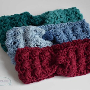 May include: Four crocheted headbands in different colors: teal, light blue, burgundy, and dark blue. The headbands are made with a textured stitch and have a slightly puffy appearance.