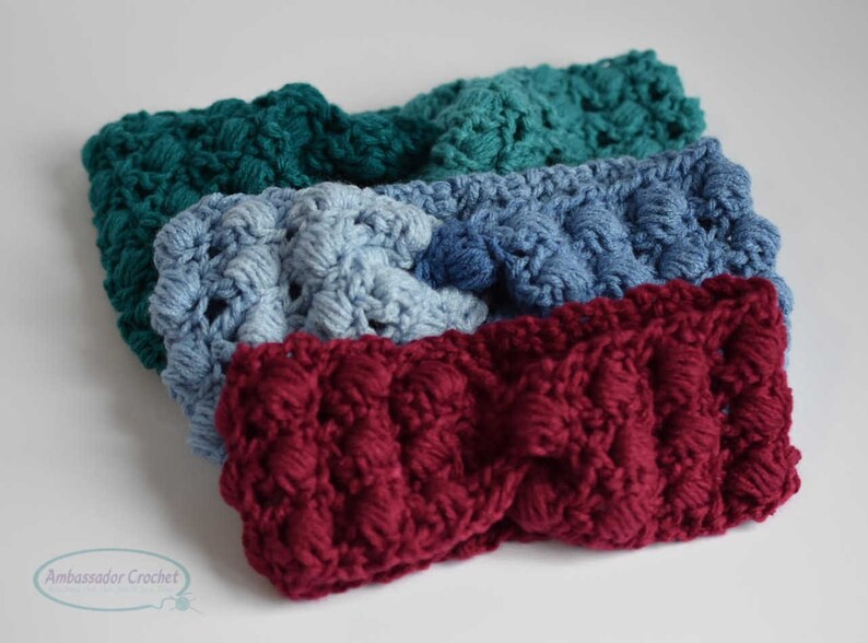 May include: Four crocheted headbands in different colors: teal, light blue, burgundy, and dark blue. The headbands are made with a textured stitch and have a slightly puffy appearance.