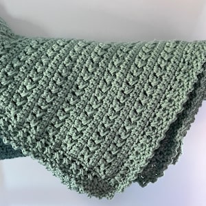 May include: A sage green crocheted blanket with a scalloped edge.