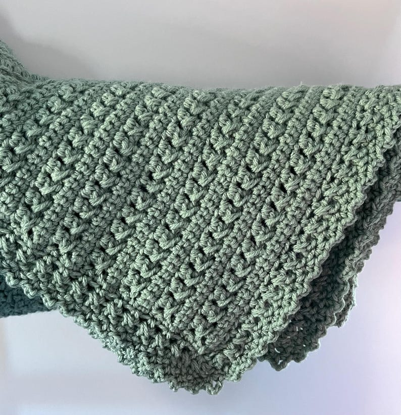 May include: A sage green crocheted blanket with a scalloped edge.