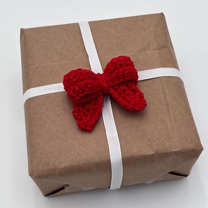 May include: A brown paper gift box with a white ribbon and a red crocheted bow.