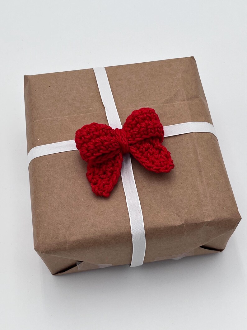 May include: A brown paper gift box with a white ribbon and a red crocheted bow.