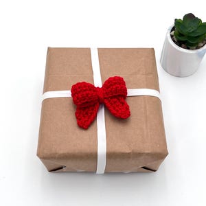 May include: A brown paper gift box with a white ribbon and a red crocheted bow.