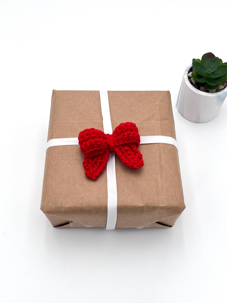 May include: A brown paper gift box with a white ribbon and a red crocheted bow.