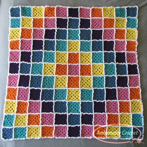 May include: A colorful, handmade crochet blanket featuring a patchwork design. The blanket is composed of numerous squares in vibrant colors including yellow, orange, pink, teal, and purple, connected by white yarn. The blanket is a square shape.