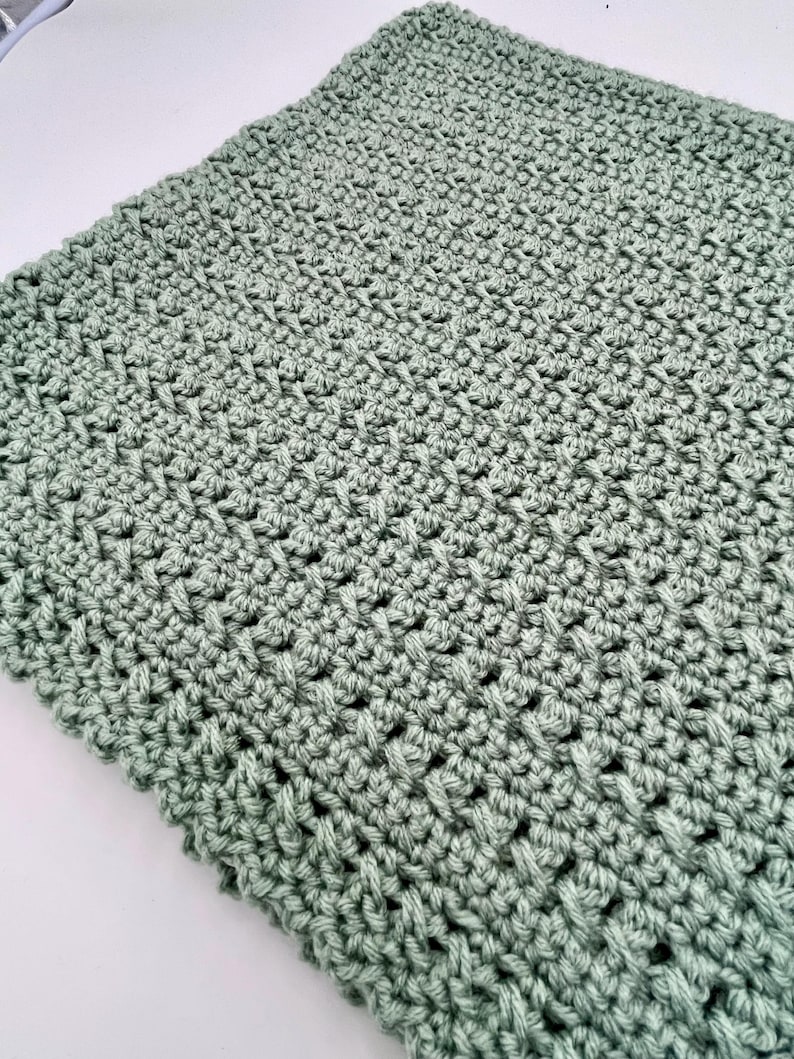 May include: A soft, sage green crocheted blanket with a textured stitch pattern.