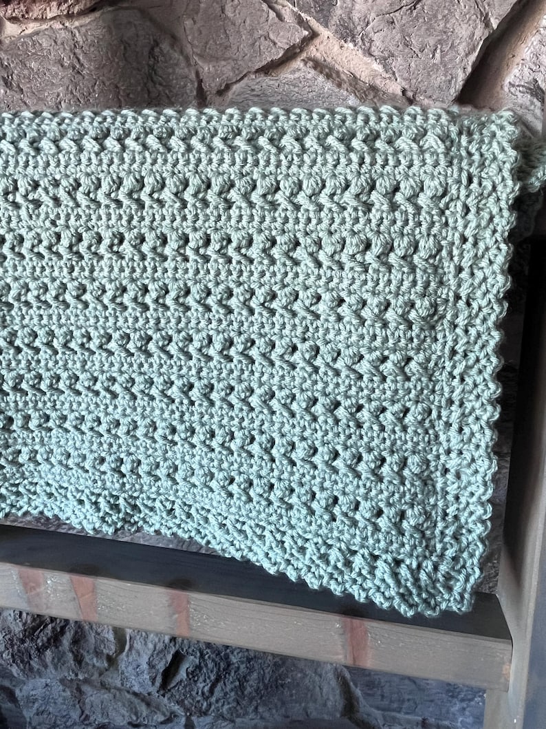 May include: A soft, sage green crocheted blanket with a textured stitch pattern.