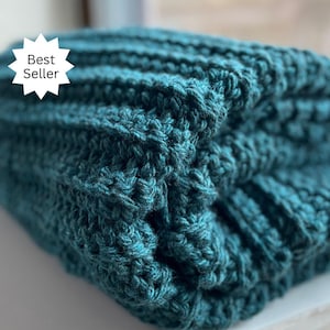 May include: A teal blue knitted blanket with a textured pattern. The blanket is folded in half and the edges are visible.