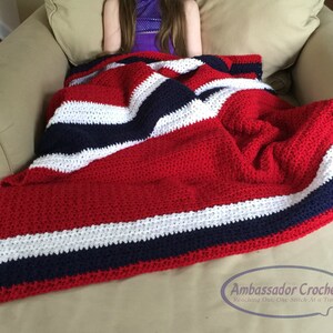 Pu&ograve; includere: Una coperta all'uncinetto fatta a mano a righe rosse, bianche e blu navy. La coperta &egrave; drappeggiata su una poltrona beige. La coperta &egrave; realizzata in filato morbido e ha un aspetto strutturato. Un accogliente elemento di arredo per la casa.