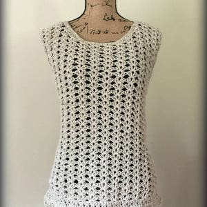 May include: A white crochet top with a sleeveless design and a scalloped hem. The top is made with an open stitch pattern, creating a lightweight and airy feel.