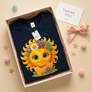 Cute cartoon sun character with big teal eyes and golden wavy rays, wearing a colorful daisy and flower crown, smiling from inside a cracked pastel pink egg covered in little hearts, with bright flowers and green grass at the base and a soft blue glowing sky behind. Playful spring and Easter graphic art, perfect for a cheerful kids T shirt design.