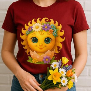 Cute cartoon sun character with big teal eyes and golden wavy rays, wearing a colorful daisy and flower crown, smiling from inside a cracked pastel pink egg covered in little hearts, with bright flowers and green grass at the base and a soft blue glowing sky behind. Playful spring and Easter graphic art, perfect for a cheerful kids T shirt design.