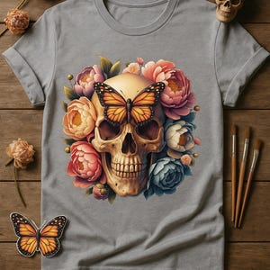 May include: Gray t-shirt featuring a skull design with a butterfly and floral elements. The skull is centered, with a butterfly on top and surrounded by colorful flowers. The butterfly is orange and black.