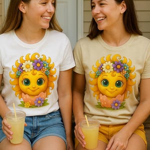 Cute cartoon sun character with big teal eyes and golden wavy rays, wearing a colorful daisy and flower crown, smiling from inside a cracked pastel pink egg covered in little hearts, with bright flowers and green grass at the base and a soft blue glowing sky behind. Playful spring and Easter graphic art, perfect for a cheerful kids T shirt design.