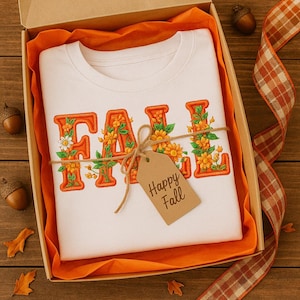 White t-shirt featuring the word “FALL” in bold vintage embroidery-style typography. Each letter is outlined in orange thread and filled with embroidered florals including daisies, blossoms, and leaves. Cozy autumn aesthetic perfect for farmhouse style, rustic outfits, or seasonal fall fashion.