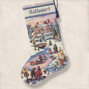 May include: Christmas stocking with a winter scene featuring a snow-covered town, bridge, and people ice skating. The top of the stocking has the name "Nathaniel" embroidered in white. A blue tassel hangs from the top.