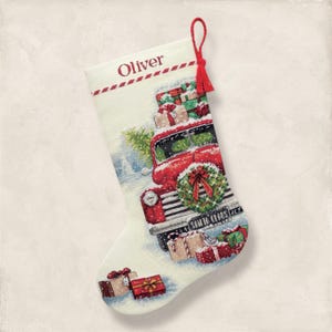 May include: Christmas stocking with a festive design. The stocking features a red truck carrying gifts and a Christmas tree. The word "Oliver" is printed at the top. A red tassel hangs from the top.