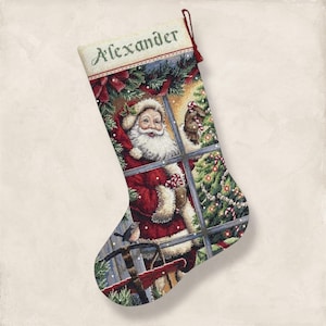 May include: Christmas stocking with a festive design, depicting Santa Claus at a window. The stocking is predominantly red and green, with the name "Alexander" embroidered on top. The scene includes a Christmas tree and a small bird.