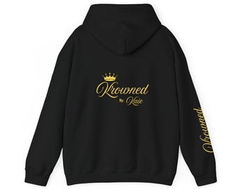 May include: Black hoodie with a hood and long sleeves. The back features gold text that reads "Krowned by Kaie" with a crown graphic. The right sleeve has the word "Krowned" in gold.