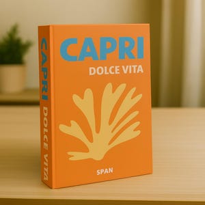 Op de afbeelding: Een oranje boek met de titel "CAPRI DOLCE VITA" met blauwe en gele tekst en een gele illustratie. Het boek staat rechtop op een lichtbruin houten oppervlak. De rug van het boek toont ook de titel en de auteur.