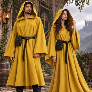 Pode incluir: Dois mantos com capuz em amarelo mostarda a combinar, com mangas compridas e largas e fecho de correr frontal. Cada manto é apertado na cintura com um cinto de couro preto com uma pequena bolsa preta presa na lateral para um visual uniforme.