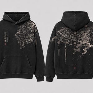 May include: A black hooded sweatshirt featuring a front and back view. The front displays a layered armor graphic and Chinese characters. The back features an intricate fan-shaped design with hanging ornaments and smoke-like patterns in grey.