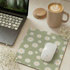 Peut inclure: Un ordinateur portable avec des autocollants de clavier à motifs de marguerites, un tapis de souris vert à motifs de marguerites et une souris blanche. Une tasse beige avec du latte art et des dessous de verre en bois.