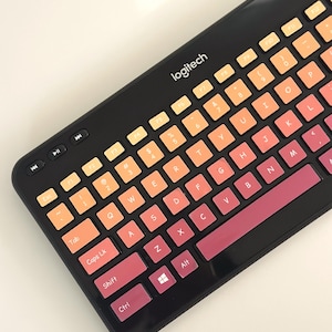 May include: Black Logitech keyboard with keys in a gradient of orange to pink. It features media control buttons and a standard QWERTY layout. The brand name "logitech" is printed on the top of the keyboard.