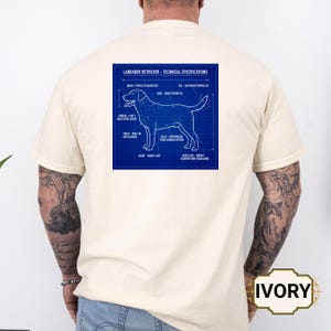 May include: Ivory t-shirt with a blue blueprint of a Labrador Retriever and technical details. The design includes labels like "Brain - People Pleaser Chip" and "Tail - Happiness Propeller". The word "IVORY" is printed on the bottom right.