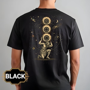 May include: Black t-shirt featuring a gold illustration of a kneeling figure supporting three large eyes. The design includes a starry background with planets and galaxies. The word "BLACK" is in a gold frame at the bottom.