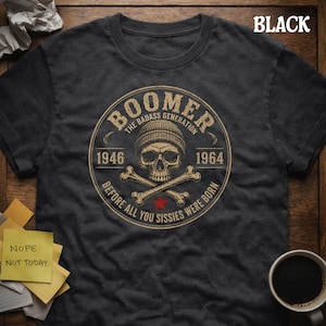 Può includere: T-shirt nera con grafica circolare raffigurante un teschio con berretto, ossa incrociate e la scritta "BOOMER The Badass Generation 1946-1964 Before All You Sissies Were Born". La parola "BLACK" è in alto.