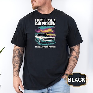 May include: Black t-shirt with a graphic of two classic cars, palm trees, and a sunset. The text reads "I DON'T HAVE A CAR PROBLEM I HAVE A STORAGE PROBLEM."