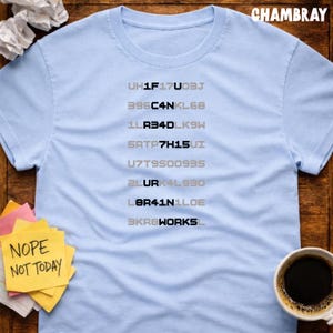 Peut inclure: T-shirt bleu clair à col rond avec une série de codes alphanumériques gris et noirs. Un post-it avec le texte "Nope Not Today" est visible. Une tasse de café est à droite.