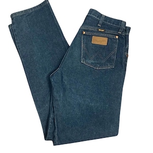 Op de afbeelding: Donkerblauwe Wrangler jeans van denim. De jeans hebben een klassiek ontwerp met vijf zakken, een bruine leren patch met het Wrangler-logo en een rechte pijp. De jeans hebben een medium wassing en lijken in goede staat te verkeren.