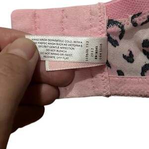 May include: Close-up of a pink bra with a leopard print lining. A white tag with care instructions is visible. The tag reads "HAND WASH SEPARATELY, COLD...RESHAPE, DRY FLAT."