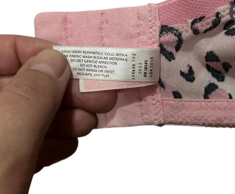 May include: Close-up of a pink bra with a leopard print lining. A white tag with care instructions is visible. The tag reads "HAND WASH SEPARATELY, COLD...RESHAPE, DRY FLAT."