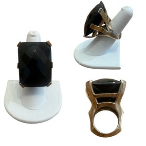 May include: Three silver rings with large, faceted black gemstones. The rings are displayed on white stands, showcasing the intricate designs and the reflective surfaces of the stones. The gemstones have a rectangular, triangular, and square shape.