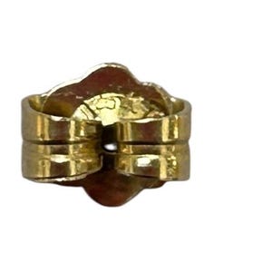 May include: A close-up of a gold-colored earring back, also known as a butterfly clutch. The earring back is made of metal and has a rounded shape with two parallel posts for securing an earring. The background is white.