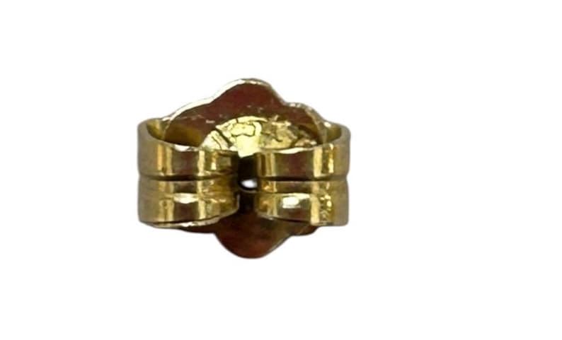 May include: A close-up of a gold-colored earring back, also known as a butterfly clutch. The earring back is made of metal and has a rounded shape with two parallel posts for securing an earring. The background is white.