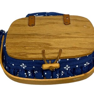May include: A blue and white fabric-lined wooden basket with a hinged lid and a wooden handle. The basket has a white floral pattern on the fabric lining.
