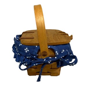 May include: A small wooden picnic basket with a blue and white floral fabric lining and a wooden handle.