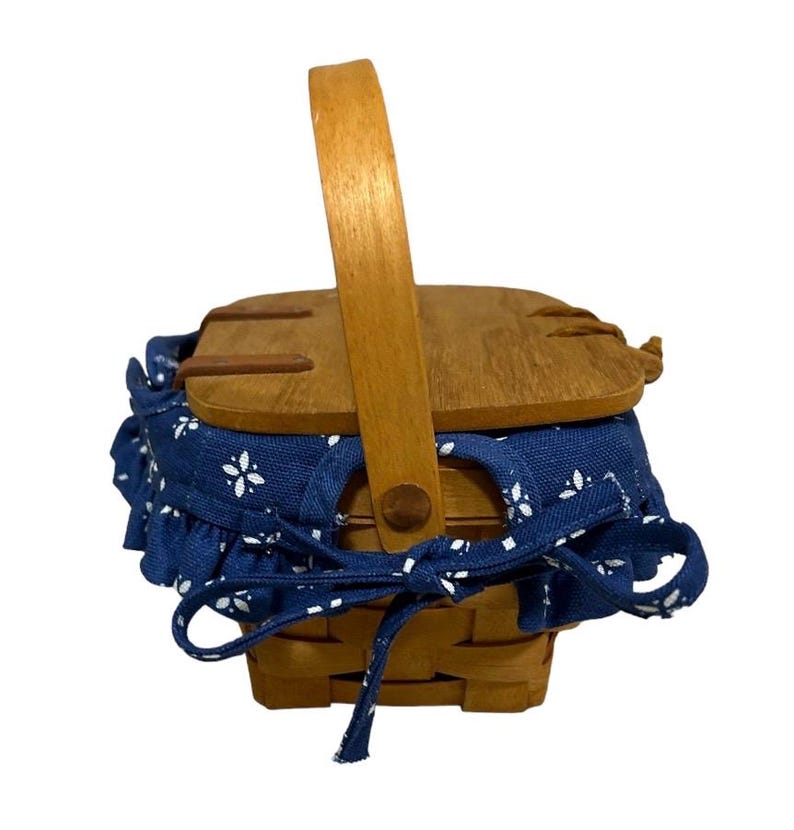 May include: A small wooden picnic basket with a blue and white floral fabric lining and a wooden handle.
