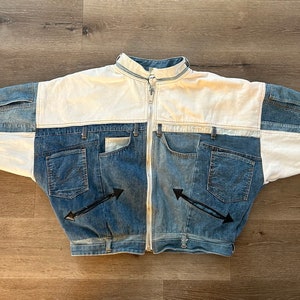 May include: A white and blue denim jacket with a zipper closure and multiple pockets. The jacket has a patchwork design with different shades of blue denim.