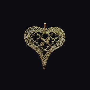 May include: A gold-colored heart-shaped pendant with a delicate, intricate design. The pendant is made of metal and has a filigree pattern.