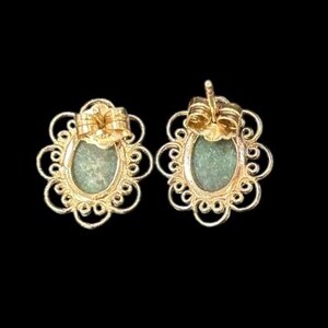 May include: A pair of gold-colored stud earrings. Each earring features an oval, light green stone set within a decorative, openwork frame. The earrings have a post and butterfly backing.