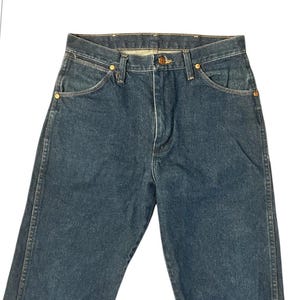 Op de afbeelding: Donkerblauwe spijkerbroek met een klassiek ontwerp met vijf zakken. De jeans heeft een knoop- en ritssluiting, koperkleurige klinknagels en een klein zakje aan de voorkant. De denim lijkt een gemiddeld gewicht te hebben.