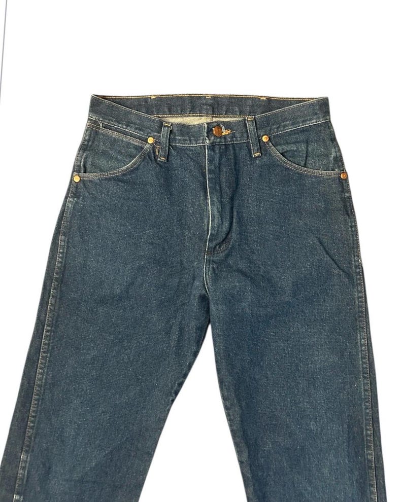 Op de afbeelding: Donkerblauwe spijkerbroek met een klassiek ontwerp met vijf zakken. De jeans heeft een knoop- en ritssluiting, koperkleurige klinknagels en een klein zakje aan de voorkant. De denim lijkt een gemiddeld gewicht te hebben.