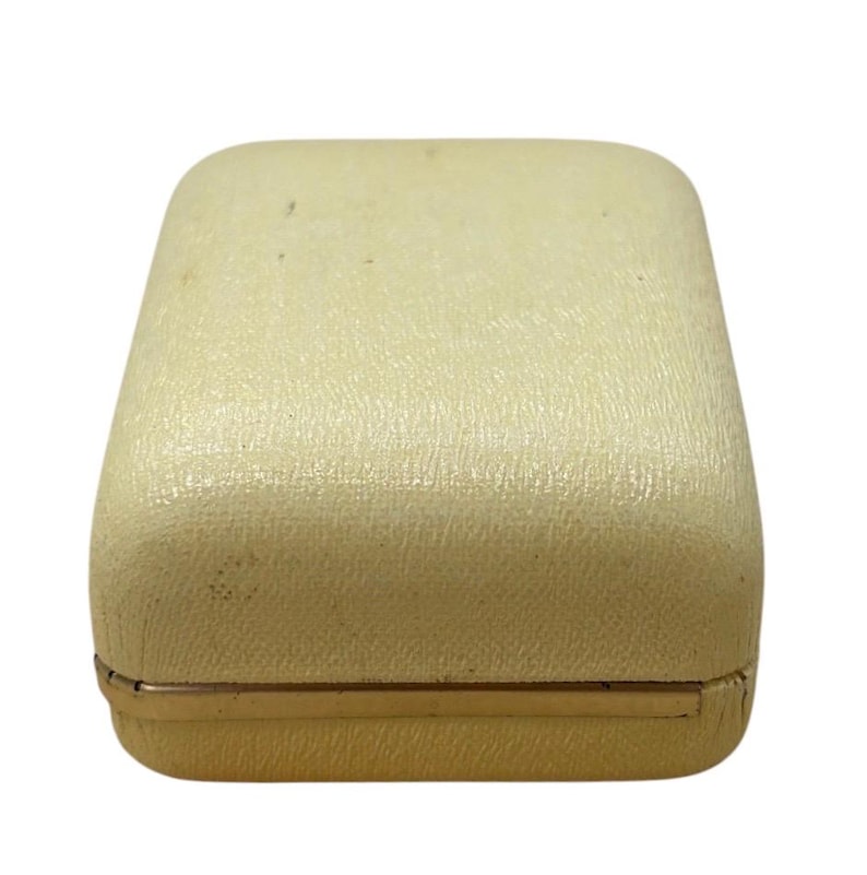 May include: A rectangular, off-white jewelry box with a textured surface. The box has a gold-colored metal trim around the base. The box is closed and appears to be empty.